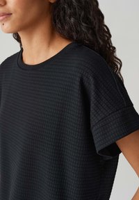 Zwart gestructureerd shirt met korte mouwen en een ronde halslijn, met een ruitpatroon en een ontspannen pasvorm. Zachte stof met een lichte stretch.