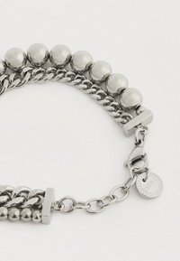 Bracciale color argento caratterizzato da due catene collegate: una con grandi perline rotonde e l'altra con perline più piccole, dotato di una chiusura a moschettone.