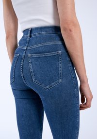 Höga blå denimjeans med fem fickor, kraftig sömnad och en figursydd design som visar en slät textur.