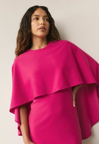 Fuksjowa sukienka z płynącym płaszczem na wierzchu, z okrągłym dekoltem i gładką fakturą. Krótkie rękawy i dopasowany krój podkreślają fason.