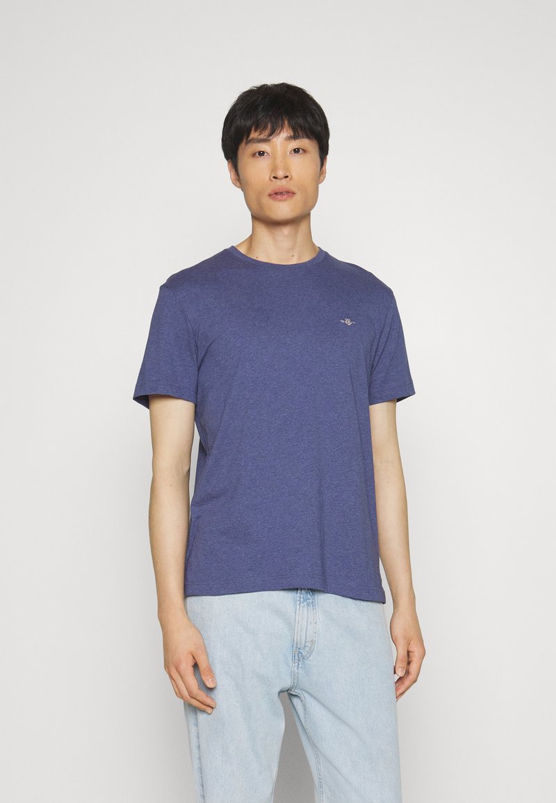 Navyblaues T-Shirt mit Rundhalsausschnitt aus weichem Stoff, mit kurzen Ärmeln und einem kleinen Logo auf der Brust. Kombiniert mit hellblauen Jeans.