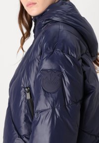 Jūras spēku puf-jaka ar kapuci, ar gumijotu logotipa uzšuvumu uz piedurknes, quilted faktūru un kontrastējošu rāvējslēdzēju.