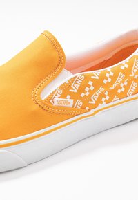 Botte de toile orange à enfiler avec des accents blancs, présente un motif à carreaux Vans sur le côté et une semelle en caoutchouc. Détails cousus présents.
