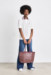 Polo shirt bianco a trama con colletto a righe, jeans blu a gamba larga e borsa bordeaux con motivo geometrico e manici doppi.