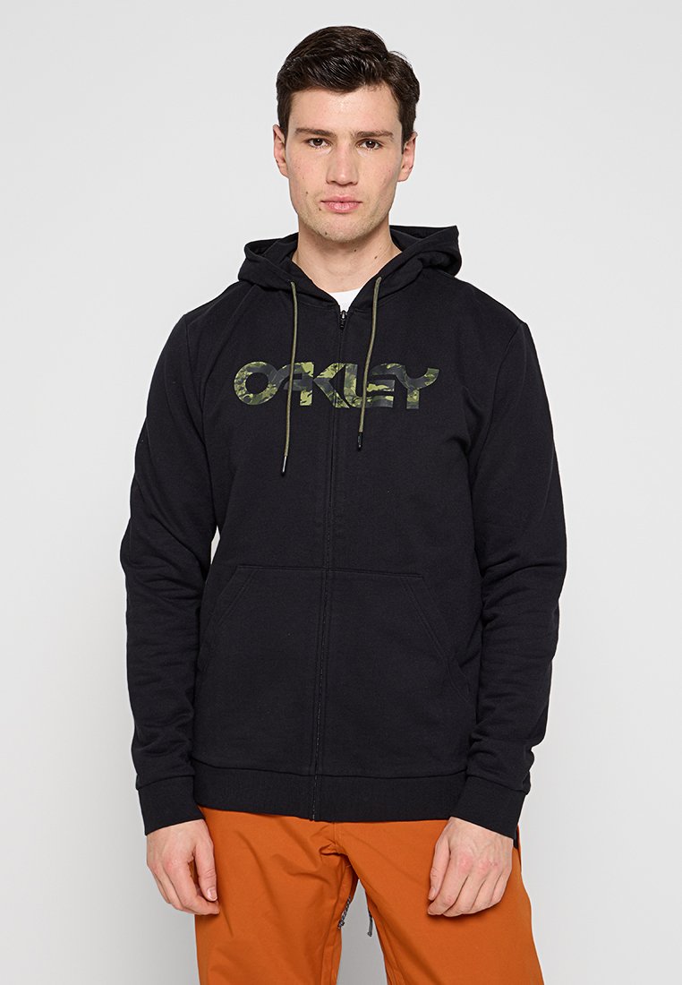 Felpa nera con zip realizzata in un mix di cotone, con logo "OAKLEY" in camouflage sul davanti, dotata di stringhe e tasche frontali.