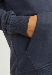 Námořnická mikina s ribovanými manžetami a klokankovou kapsou. Hladký povrch, ležérní design a kontrastné švy v blízkosti kapsy.