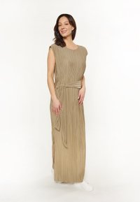 Beige pleated maksimekko, jossa on lyhyet hihat, vyöllinen vyötärö ja sivuaukot. Sileä pinta, lattiaan asti ulottuva malli, yhdistetty valkoisiin tennareihin.
