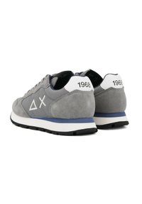 Sneakers in camoscio grigio con dettagli bianchi, caratterizzati da un logo triangolare e "1968" in rilievo sul tallone. Suola in gomma nera e linguetta imbottita.