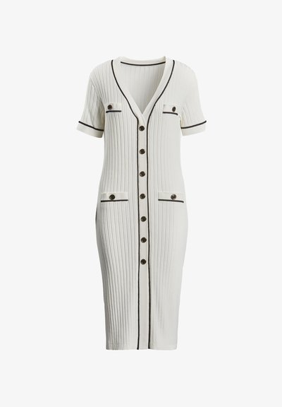 Fehér, fekete díszítéssel ellátott bordázott kötött ruha, rövid ujjú, V-nyakú, elöl gombos záródással és két zsebel. A gombok kör alakúak.