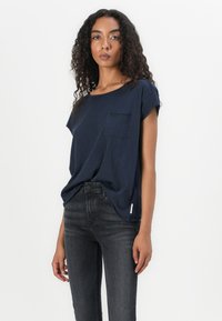 Camiseta de manga corta en azul marino con bolsillo en el pecho, corte relajado y tela suave, combinada con vaqueros skinny oscuros.