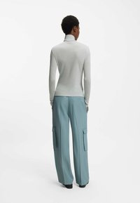 Light gray long-sleeve turtleneck paired with loose, high-waisted teal cargo pants featuring large side pockets and a smooth texture.