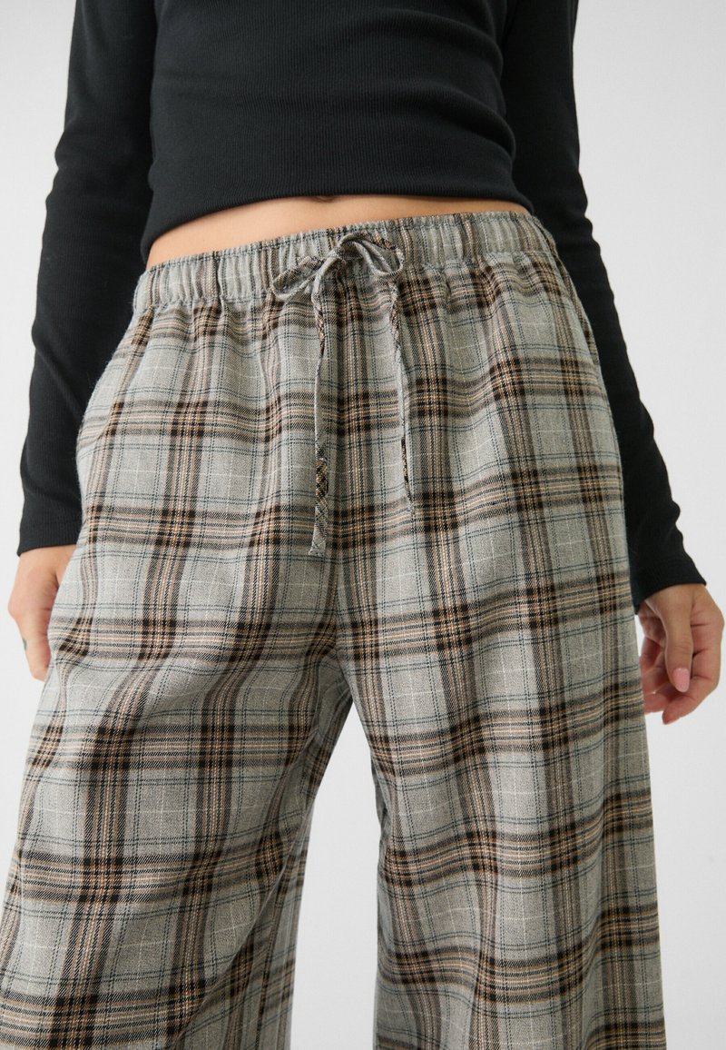 Graue Karohosen verfügen über einen elastischen Taillenbund mit Kordelzug und einen weiten Schnitt. Der Stoff hat eine weiche Textur mit braunen und schwarzen Akzenten.