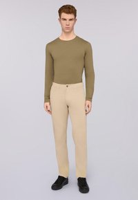 Camisa de manga larga verde oliva combinada con pantalones beige claros, con cierre de botón, llevada con zapatillas negras. Textura suave.