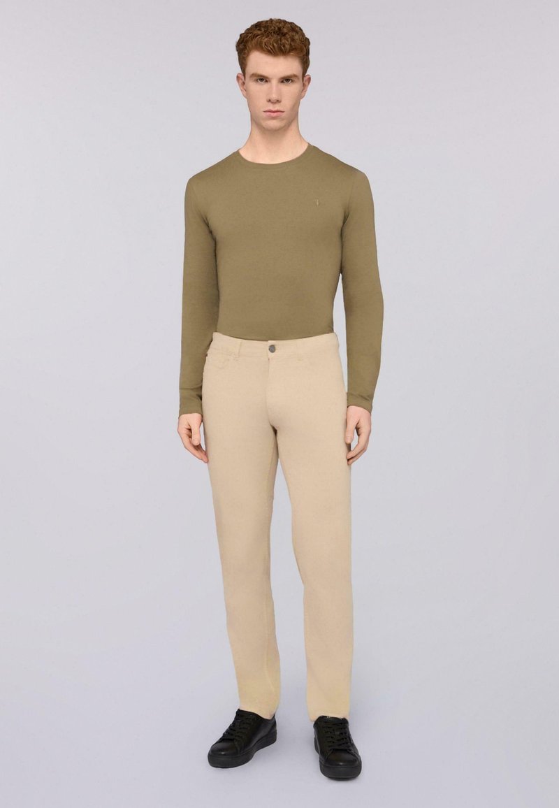 Camisa de manga larga verde oliva combinada con pantalones beige claros, con cierre de botón, llevada con zapatillas negras. Textura suave.