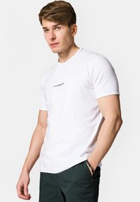 Biała, krótko-sleeve t-shirt z miękkiego materiału, z okrągłym dekoltem i czarnym logo "LANCERTO" na piersi, zestawiona z ciemnozielonymi spodniami.
