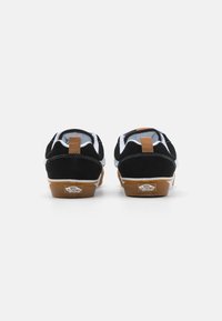 Sneakers negri din suede cu accente albe și o talpă din cauciuc de culoare caramel, având un tab de călcâi maro și un detaliu cu logo pe spate.