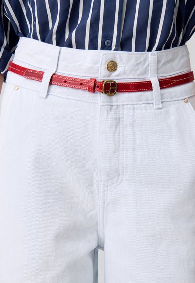 Pantalones de mezclilla azul claro con cintura alta presentan un cinturón de cuero rojo. El cinturón tiene una hebilla redonda de oro y costuras visibles que acentúan el diseño.