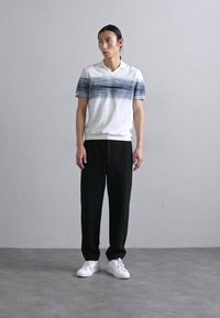 Λευκό και μπλε ριγέ πόλο μπλούζα με κολάρο, συνδυασμένη με μαύρο παντελόνι και λευκά αθλητικά παπούτσια. Απλός σχεδιασμός και άνετη εφαρμογή.