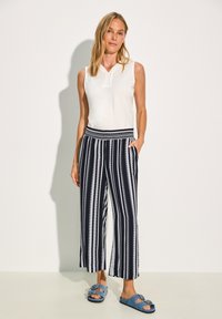 Vit ärmlös topp med v-ringning, kombinerad med navy och vita randiga culottebyxor med elastisk midja och två sidofickor.