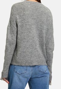 Szary sweter z dzianiny o luźnym kroju, z prążkowanymi mankietami i obrębem oraz miękką teksturą. Połączony z niebieskimi dżinsami.