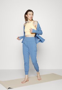 Calças de ioga texturizadas azul claro e um cardigã com um top cropped amarelo. O conjunto apresenta um design casual com bolsos e mangas ajustadas.