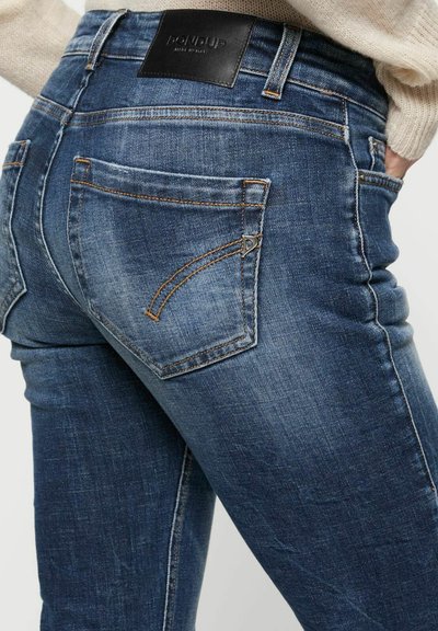 Jeans bleu foncé en denim, présentant une coupe slim, un léger délavage, des surpiqûres contrastées et une étiquette en cuir sur la taille.