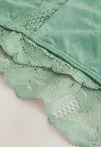 Myntegrønt stof med fint blonderkant med bølgede kanter og indviklede mønstre. Glat tekstur med detaljerede syningsdetaljer.