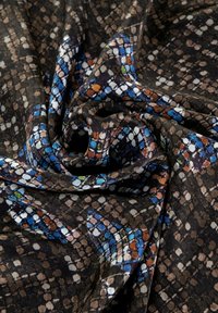 Tessuto in nero con un design multicolore e geometrico che presenta cerchi e rettangoli in blu, arancio e bianco. Tessitura morbida e drappeggiata.