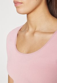 Top de color rosa claro con canalé, escote redondeado, ajuste ceñido y textura suave, mostrando una vista de cerca del tejido y los detalles del diseño.