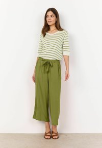 Zelené široké kalhoty s elastickým pasem v kombinaci s pruhovaným svetry v světle zelené a bílé barvě ve tvaru V. Hnědé sandály outfit dokončují.