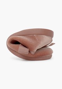 Zapatilla de tela suave en color rosa, con suela redondeada, diseño plegado, material texturizado y un pequeño lazo para facilitar poner y quitar.