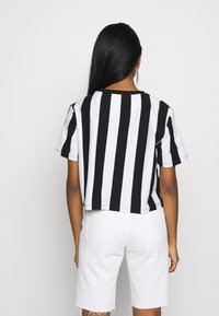 Camiseta corta a rayas blancas y negras con mangas cortas y cuello redondo, combinada con pantalones cortos blancos. Material de mezcla de algodón.