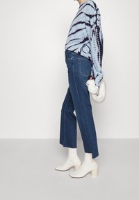 Light blue tie-dye long-sleeve shirt, blue denim high-waisted straight-leg jeans, and white ankle boots with block heels. White handbag held.