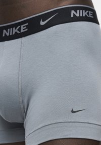 Κοντινό πλάνο γκρι ανδρικών εσωρούχων Nike με μαύρη ζώνη μέσης που φέρει γκρι λογότυπο Nike και σβούρα στο πλάι του ποδιού.