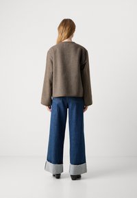 Brun tekstureret sweater med brede ærmer parret med højtaljede, løse blå jeans med slidte grå manchetter. Model set fra bagen.