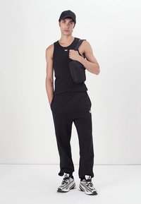 Sort tanktop og træningsbukser, parret med en lille sort crossbody taske. Sneakers har en blanding af hvide og sølv accenter.
