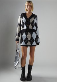 Sort og hvid argyle sweaterkjole med V-udskæring, tre knapper og lange ærmer. Tekstureret garn og tætsiddende silhuet. Sølv taske.