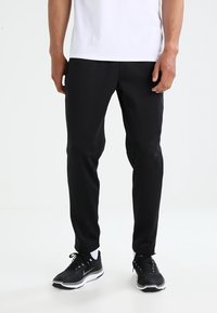 Black athletic pants with a slim fit, made of lightweight material. Features subtle seam details and paired with black athletic shoes.