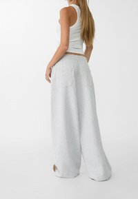 Lichtgrijze, brede sweatpants met een elastische tailleband en twee achterzakken. De stof lijkt zacht met een gladde, licht gestructureerde afwerking.