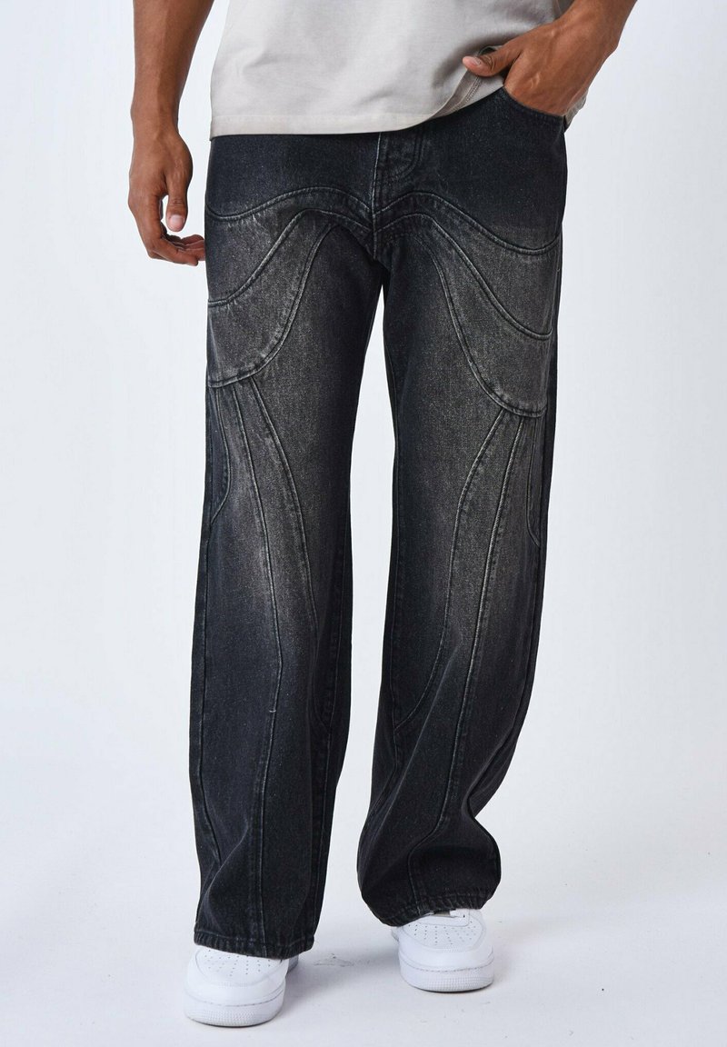 Jeans en denim noir avec une coupe décontractée, présentant des détails de couture courbée, une texture légèrement distendue et une taille positionnée au-dessus des hanches.