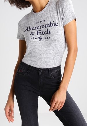 Harmaa lyhythihainen t-paita, jossa tummansininen painatus "Abercrombie & Fitch New York," yhdistettynä mustiin istuviin farkkuihin. Sileä pinta, rento istuvuus.