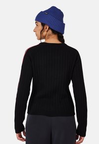 Schwarzer gerippter Pullover mit langen Ärmeln, versehen mit roten Seitenstreifen. Begleitet von einer blauen gestrickten Mütze, die einen strukturierten Stoff zeigt.