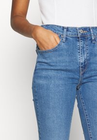 Jeans in denim blu a vita alta con una trama liscia, dotati di tasche frontali e un dettaglio di cucitura a contrasto lungo le cuciture.
