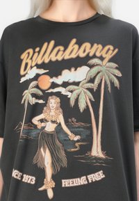 Svart bomull T-skjorte med fargerik retro grafikk av en hula danser, palmer og solnedgang. Teksten sier "Billabong" og "Feeling Free."