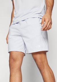 Lys blå shorts laget av lett materiale, med sidelomme, rett kant, og en liten hvit logo på venstre bein.