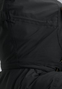 Zwarte jas met een gestructureerde stof, zichtbare stiksels en een getailleerd ontwerp. Bevat een zak en verstelbare hardware accenten.