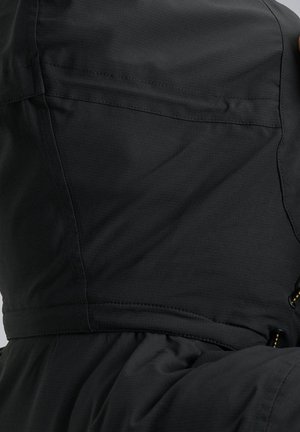 Zwarte jas met een gestructureerde stof, zichtbare stiksels en een getailleerd ontwerp. Bevat een zak en verstelbare hardware accenten.