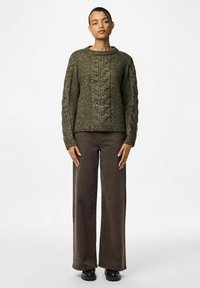 Oliivroheline kudumissvett, millel on nööbivarrukad ja tekstuuriga paneelid, koos laia jala pruunide pükstega. Sile kangaste viimistlus, mugav lõige.