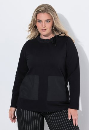 Black sweatshirt with a ruffled neckline and two front pockets, featuring a smooth texture. Styled with striped black pants.