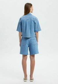 Giacca di jeans con maniche corte, design cropped e colore azzurro chiaro abbinata a pantaloni corti coordinati. Entrambi presentano una texture liscia e una semplice cucitura.